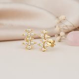gold spike stud earrings with round stones on a cream backdrop with dried flowers and a rose quartz stone