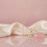 gold lariat necklace with stone stations on a pink backdrop with dried baby's breath and a rose quartz stone