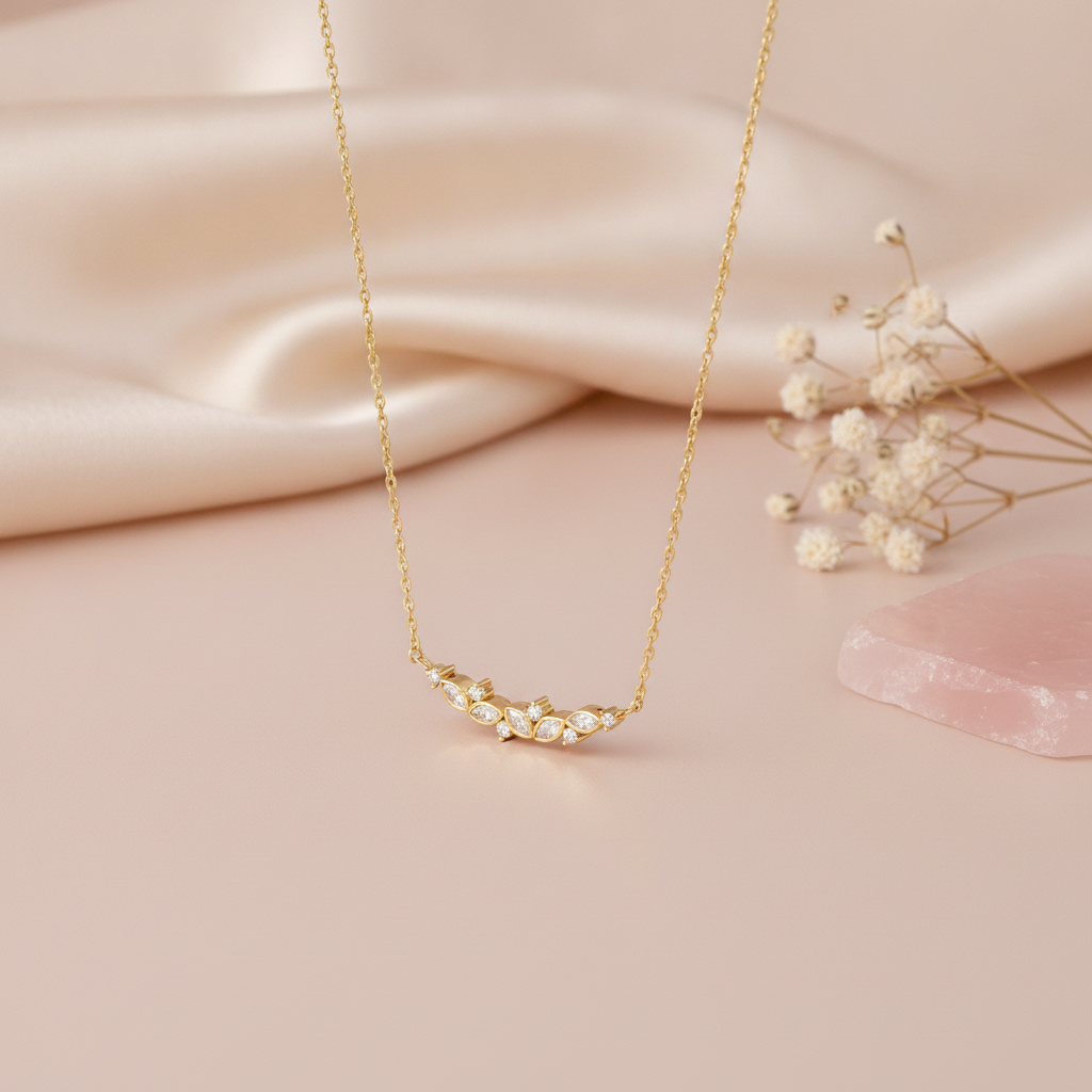 gold necklace with a curved arc of marquise stones on a pink backdrop with dried flowers and a rose quartz stone