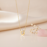 gold circle pendant necklace with a round center stone on a cream backdrop with dried baby's breath and a rose quartz stone