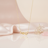 gold ribbon knot necklace displayed on blush satin with dried baby's breath and a rose quartz stone