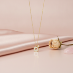 gold pave square pendant necklace displayed on blush satin with a dried rose and a pink stone