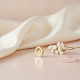 gold circle halo pendant necklace displayed on blush and cream satin with dried baby's breath and a pink stone