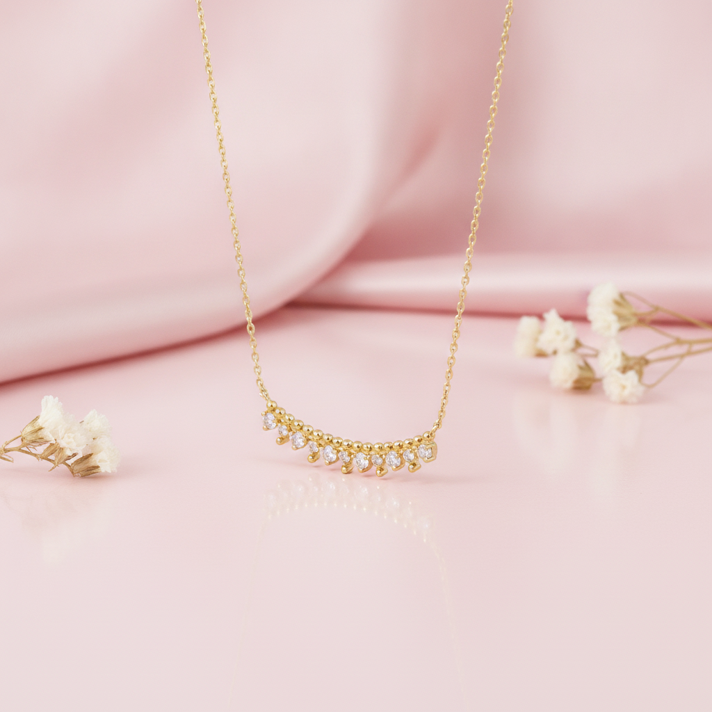 gold beaded arc necklace with fringe stones displayed on blush satin with dried baby's breath