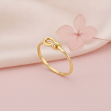 gold knot ring displayed on pink satin with a dried pink flower